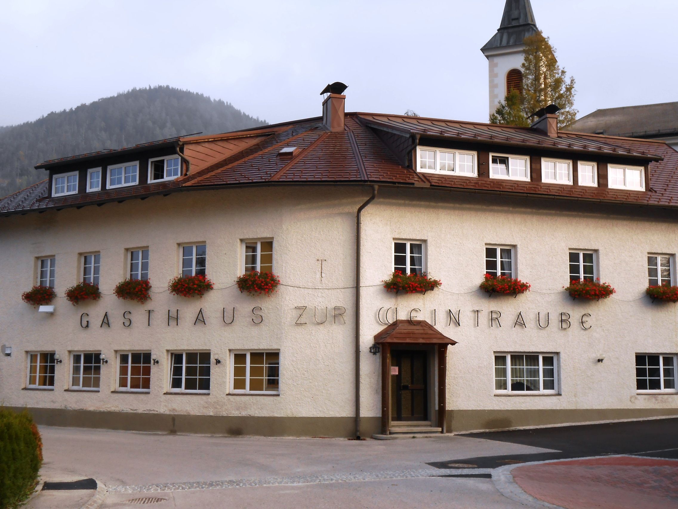 A traditional inn with flowers in the windows and a church tower in the background.
