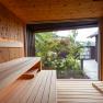 Interior view of a modern sauna with wooden walls and benches, view of a garden through a large window.