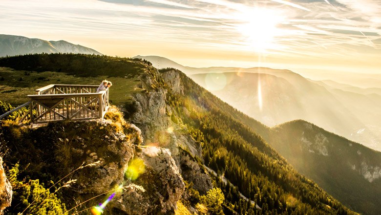 Viewing platform on a mountain with a view of wooded hills and sunset.
