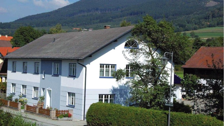 Private room family Karl, © Privatzimmer Familie Karl A large, two-storey, white and blue house with a garden and mountain landscape in the background.
