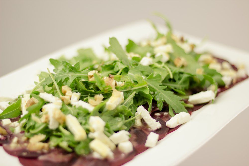 A plate with rocket, cheese and nuts on thin slices of meat.