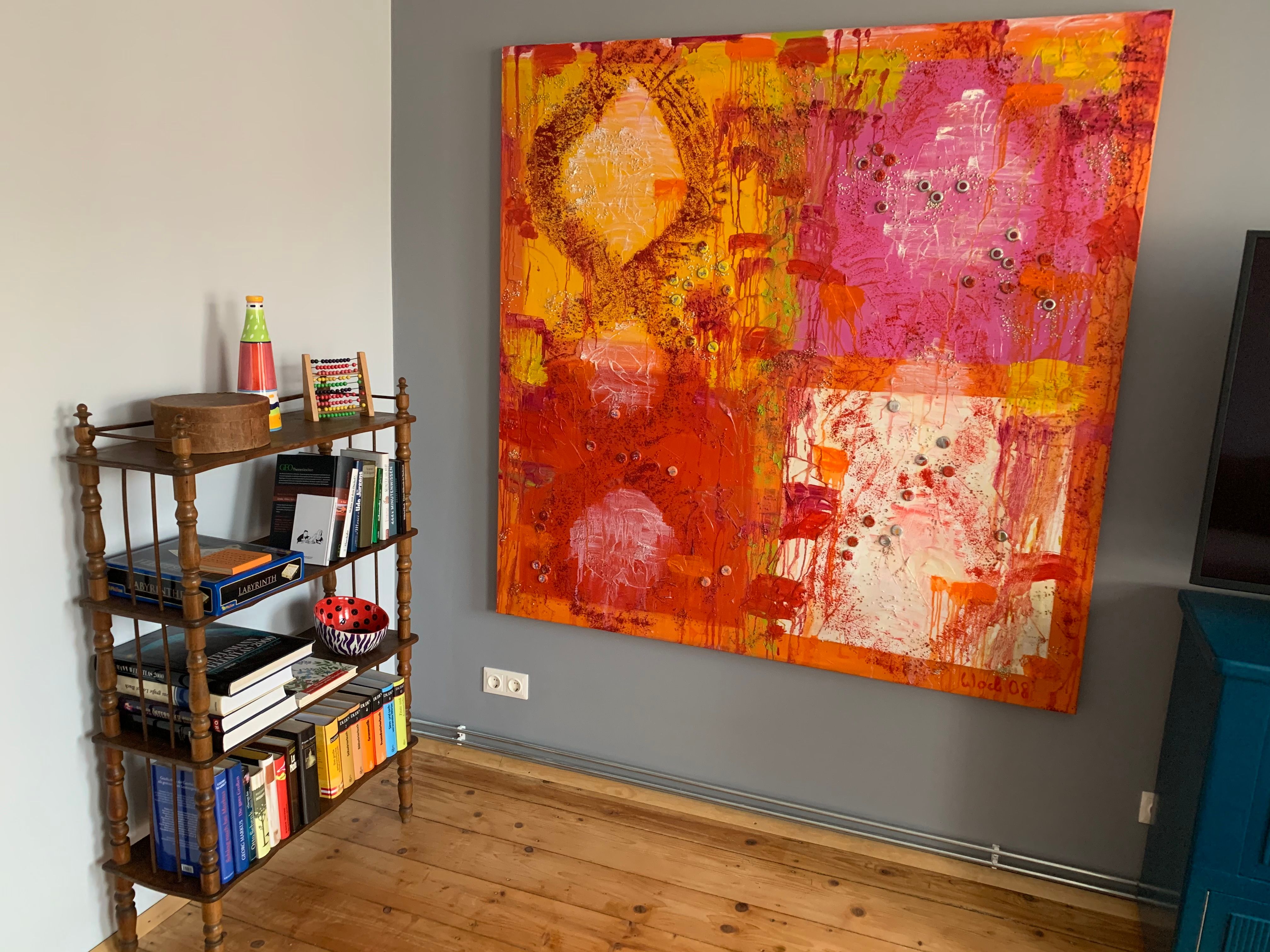 A small bookshelf with books and decorations next to a large, colorful painting on the wall.