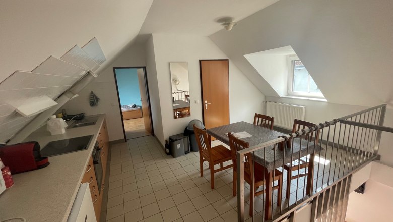 Kitchen-cum-living room with dining table, chairs, kitchenette and sloping roof.