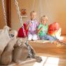 Two children sit on a swing in a play area with sandbags and beanbags.