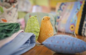 Two fabric birds, one green and one orange, on a table with fabrics and sewing utensils.
