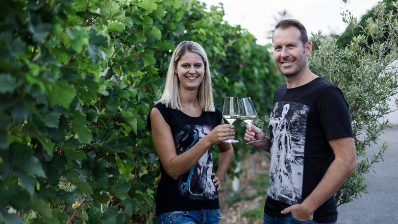 Two people clink glasses in a vineyard.