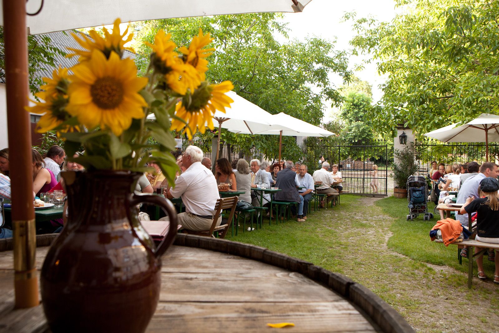 A beer garden with people at tables, parasols and sunflowers in a jug in the foreground.