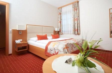 A cozy hotel room with a double bed, red carpet and floral decorations on a table.