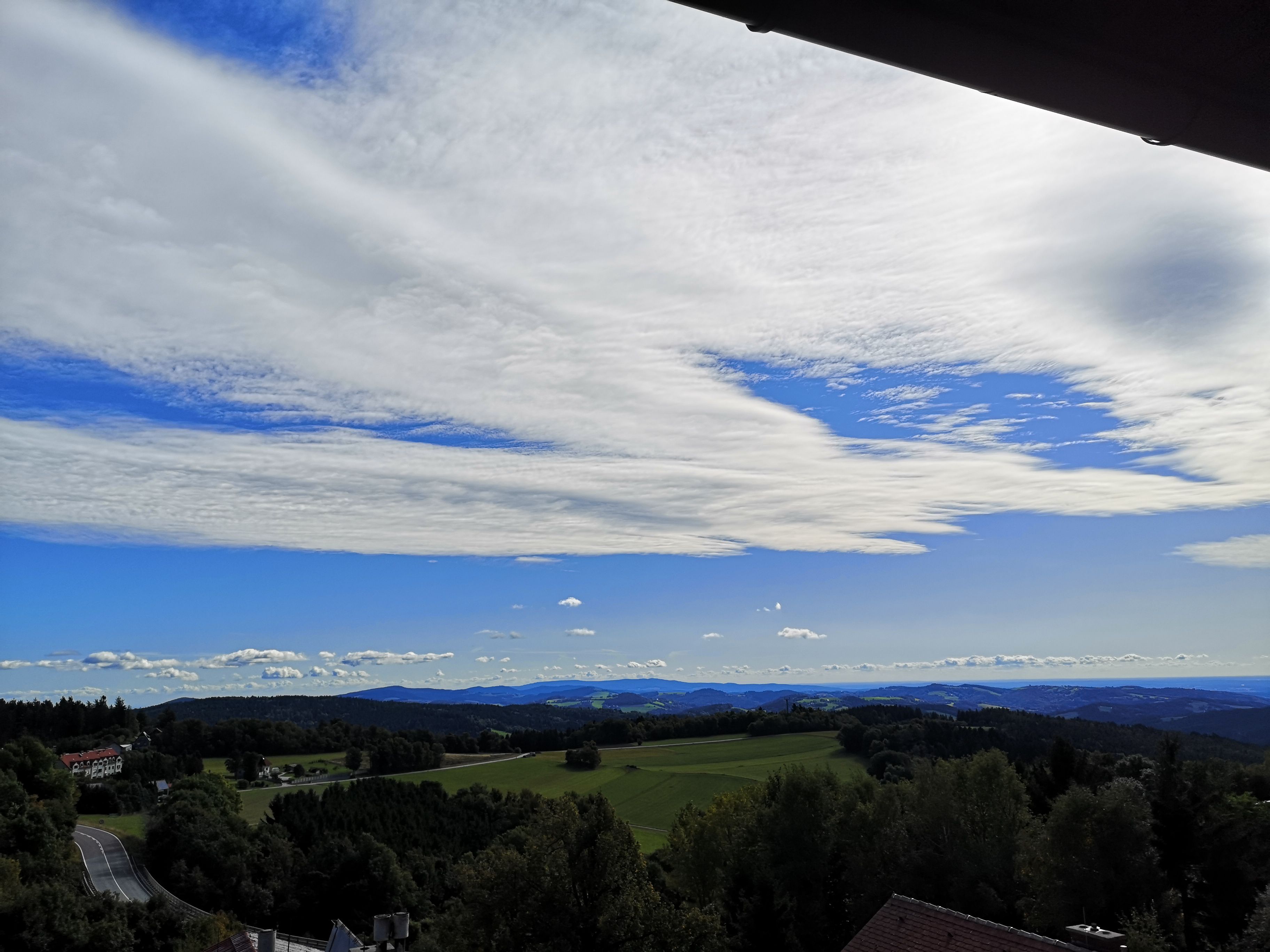 Landscape with hills, forests and a wide sky with clouds.