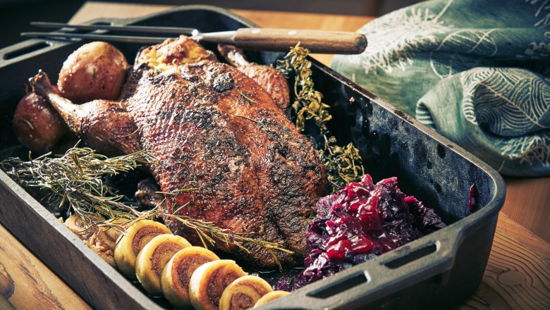 Roasted goose with side dishes in a roasting tin.