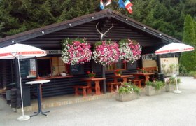 Wooden hut with flowers and parasols in front of a forest.