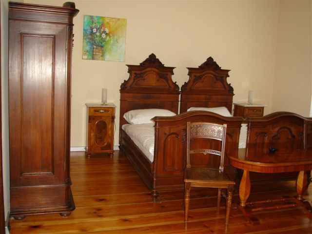 A traditionally furnished bedroom with antique wooden furniture, including two beds, a wardrobe and a table.