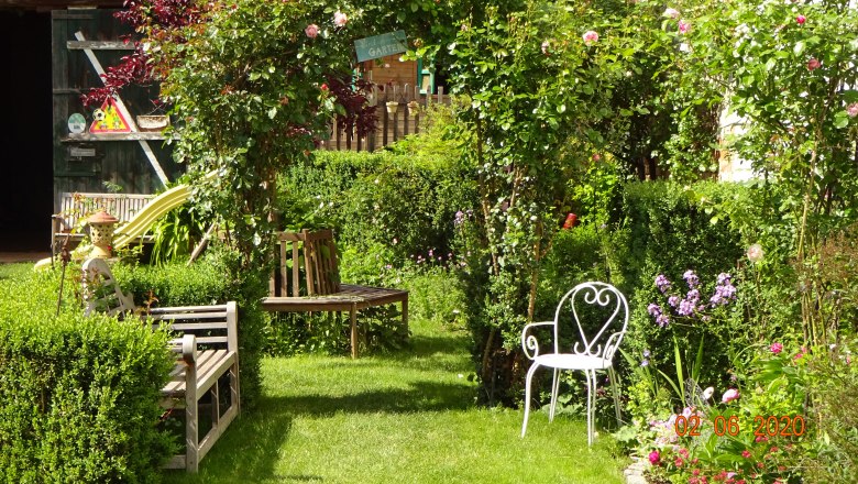An idyllic garden with benches, a white chair and flowering plants.