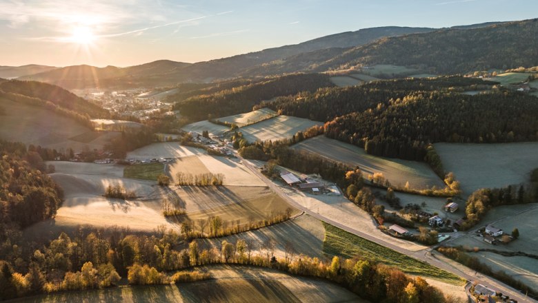 Aerial view of a rural landscape at sunrise with fields, forests and scattered buildings.
