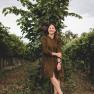 A woman stands smiling in a vineyard in front of a grapevine.