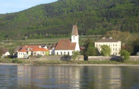 Hofarnsdorf parish church with surrounding buildings and wooded hill in the background, taken from the Danube.