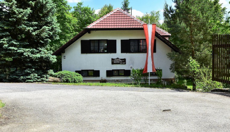 A warm welcome!, © Waldcamping Hubertus A white house with a red roof and an Austrian flag in front of it, surrounded by trees.