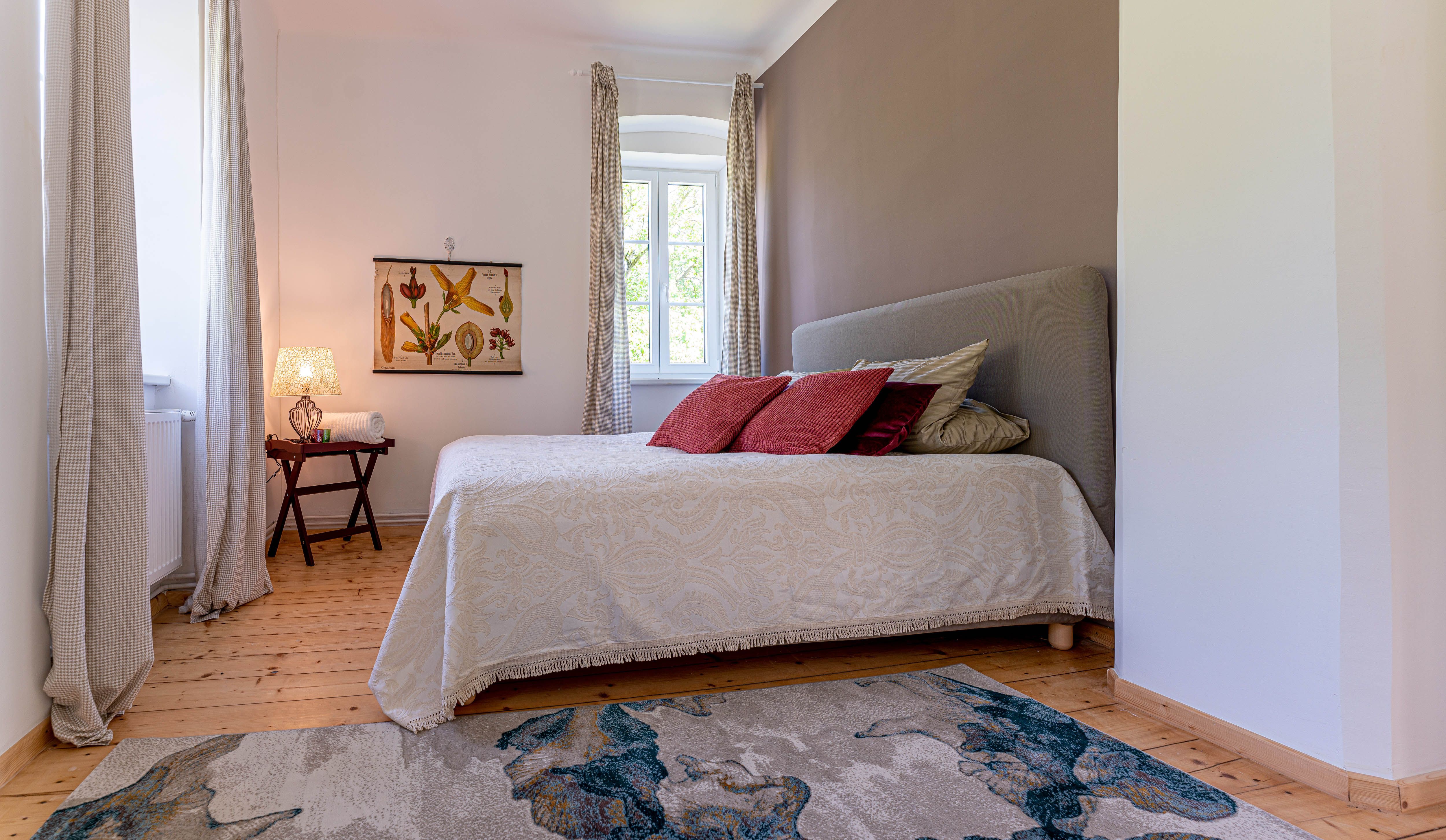 Bedroom with bed, red cushions, carpet and window with curtains.
