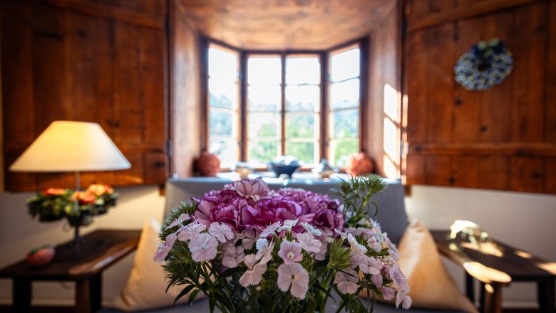 A cozy living room with wood paneling, a window with a view outside and a bouquet of flowers in the foreground.