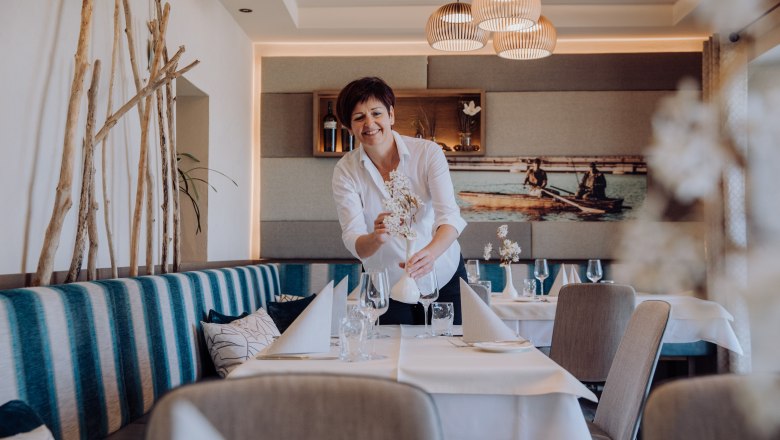 A woman in a restaurant arranges flowers on a table.