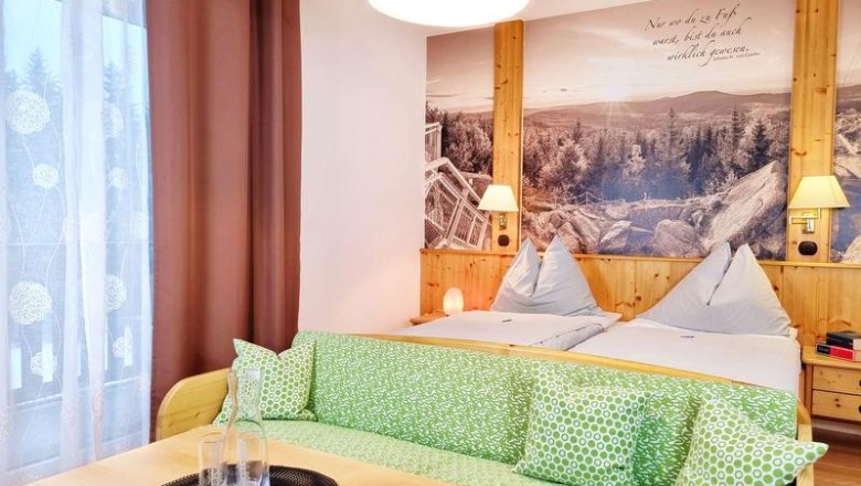 Cozy double room with two beds, green sofa and large mural of a landscape.