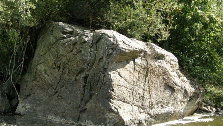 Large rock on the bank of a river, surrounded by trees.