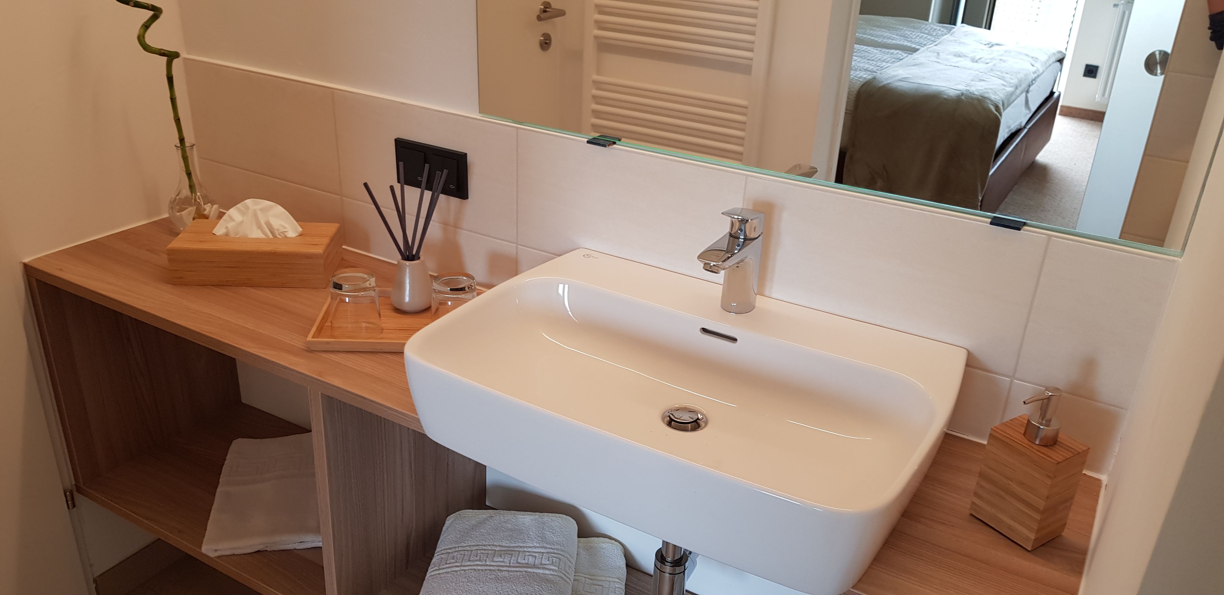Modern bathroom with washbasin, mirror and wooden shelf.