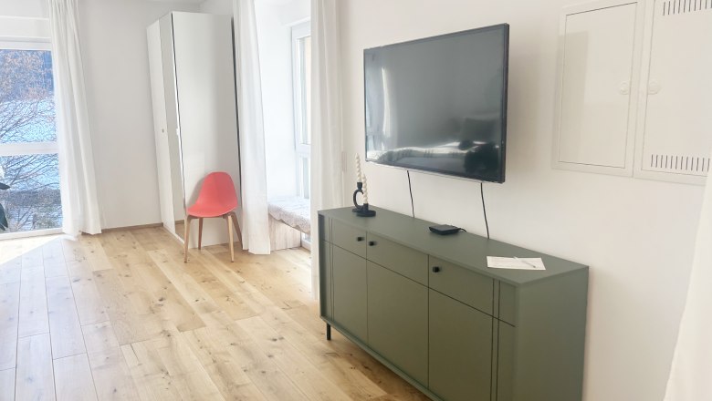 Modern living room with wooden floor, green sideboard, wall-mounted TV and red chair in front of a mirror.