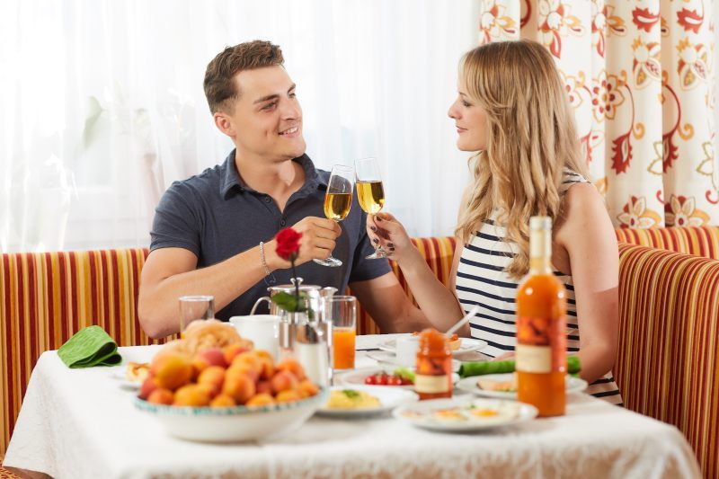 A couple toast with champagne glasses at breakfast, surrounded by fruit and drinks on a laid table.