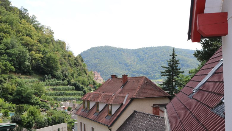 View of a village with red roofs and green hills in the background.