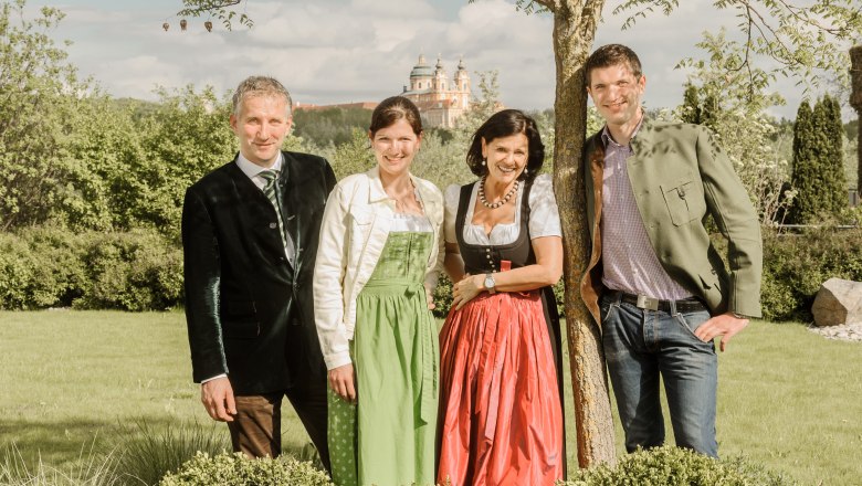 The Pichler family in traditional dress stand outside in front of a tree, with Sift Melk in the background