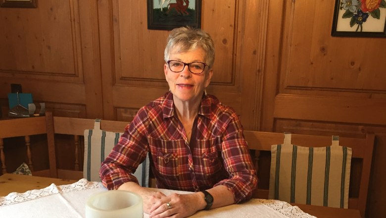 A woman sits at a table with a white tablecloth in a wood-paneled room.