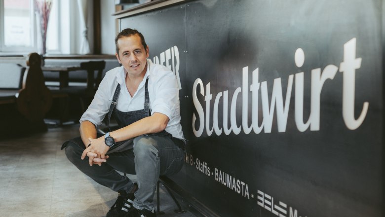 A man in work clothes squats in front of a sign that reads 'Stadtwirt'.