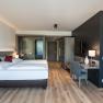 Modern hotel room with double bed, desk and wooden floor.