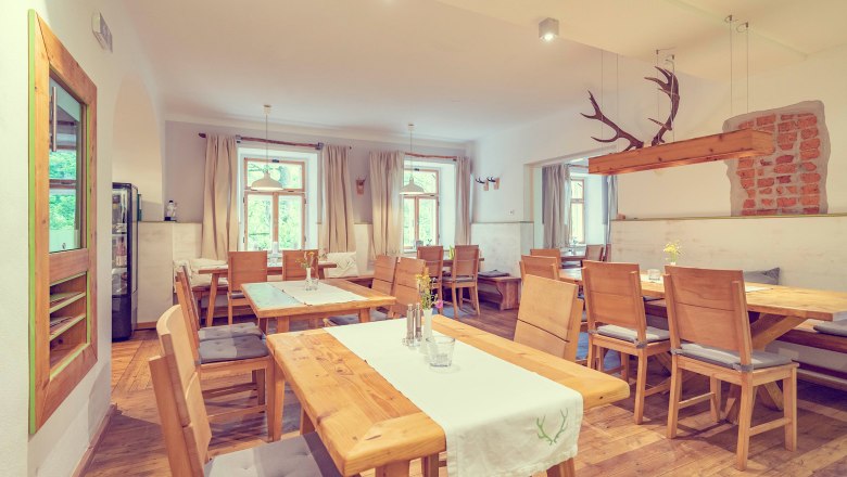 A rustic-modern room with wooden furniture, white walls and large windows. Antlers hang from the ceiling as decoration.