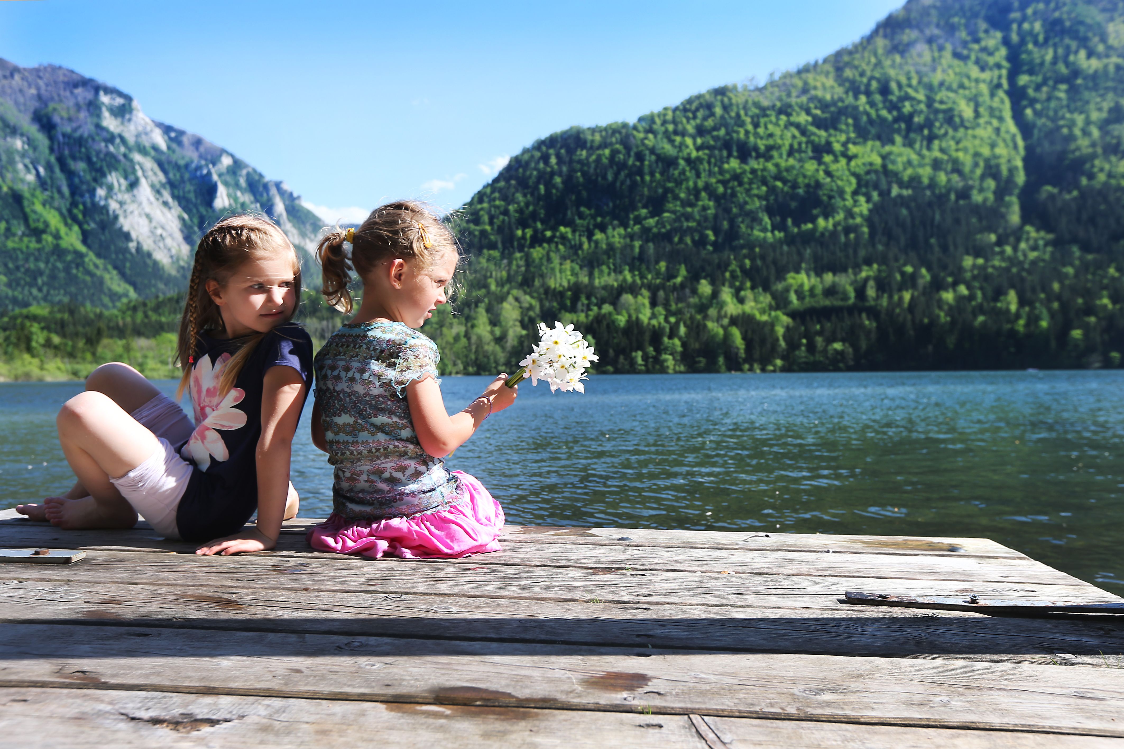 Two children sitting on a jetty on Lake Lunz with mountains in the background.