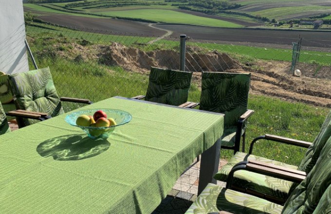 Terrace with green table and chairs, view of fields and hills.
