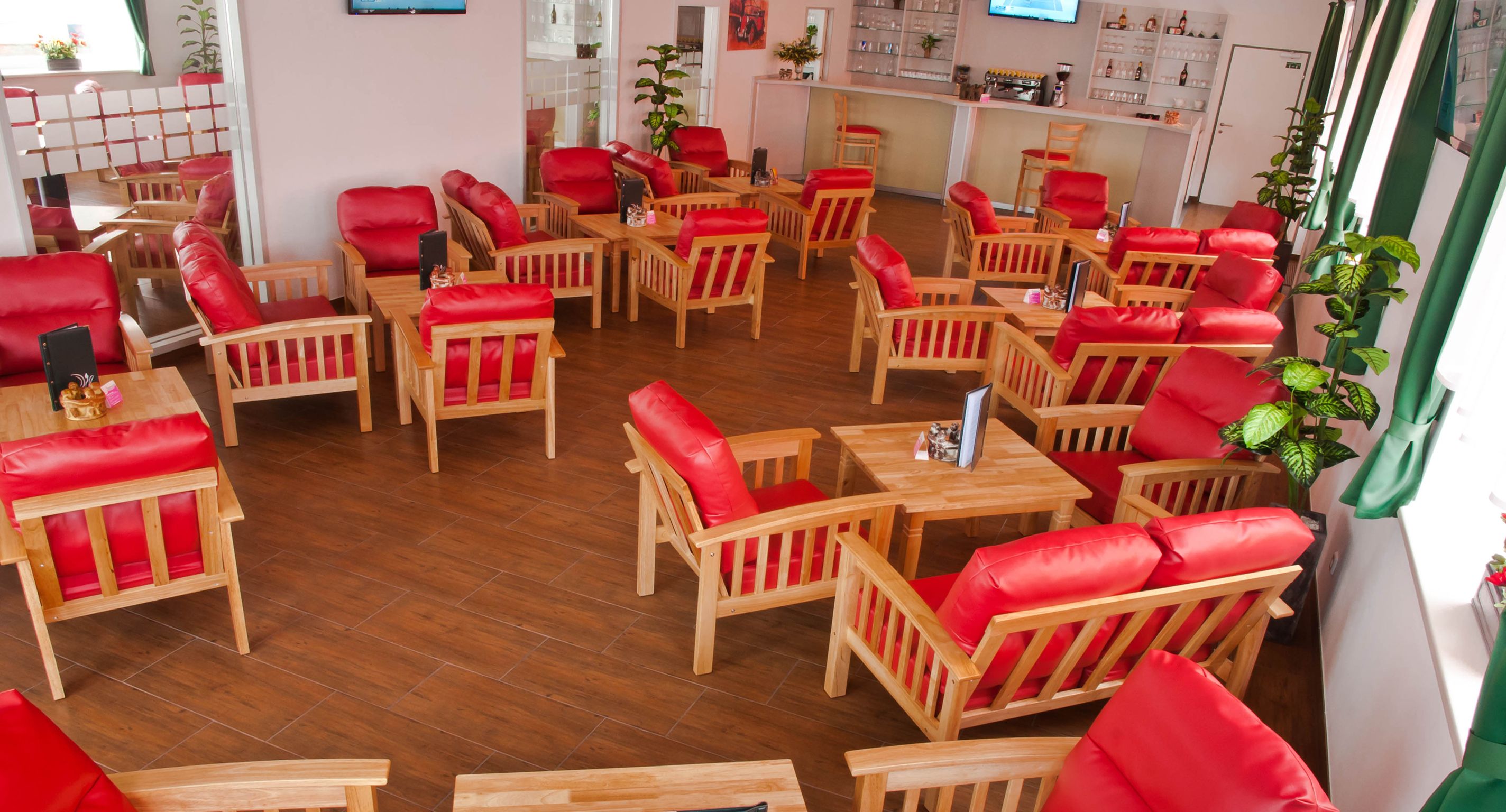 A lounge with red armchairs and wooden tables on a wooden floor.