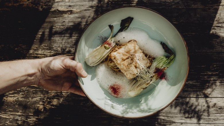 A plate with an artfully arranged dish consisting of baked fish, noodles and vegetables on a wooden table.