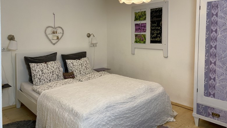 Cozy double room with white bed, decorative heart shelf and purple wardrobe.