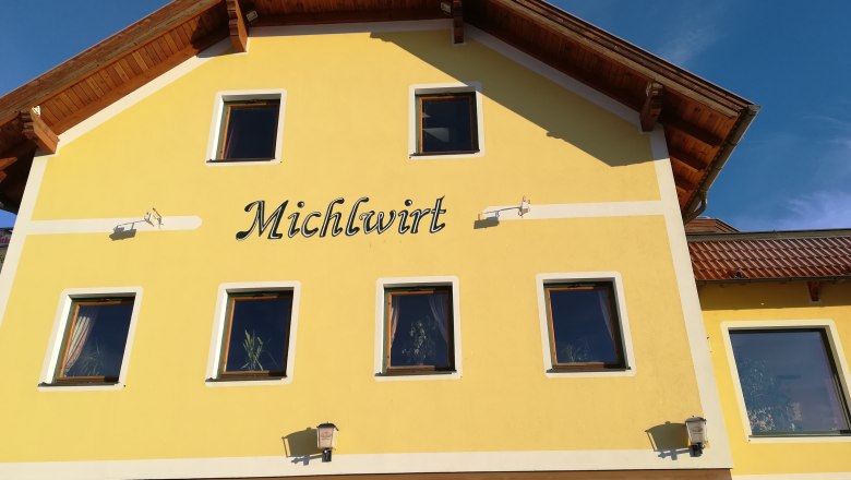 Yellow building with the inscription 'Michlwirt' and several windows, under a blue sky.