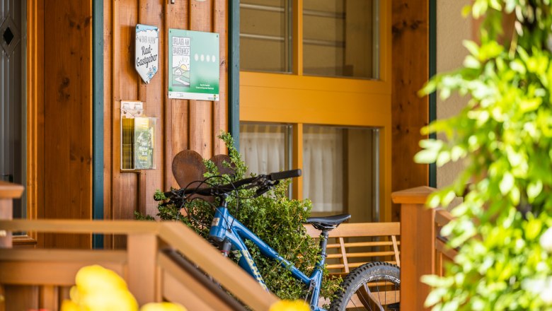Entrance area of a building with wooden cladding, bicycle and signs.