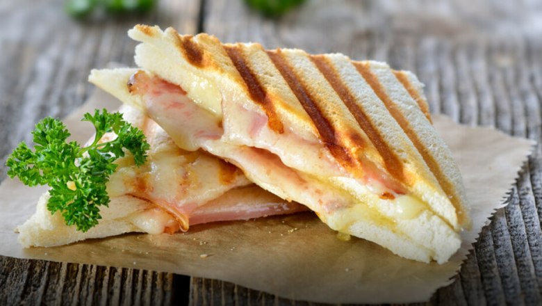 A grilled sandwich with ham and melted cheese, garnished with parsley, on a wooden board.