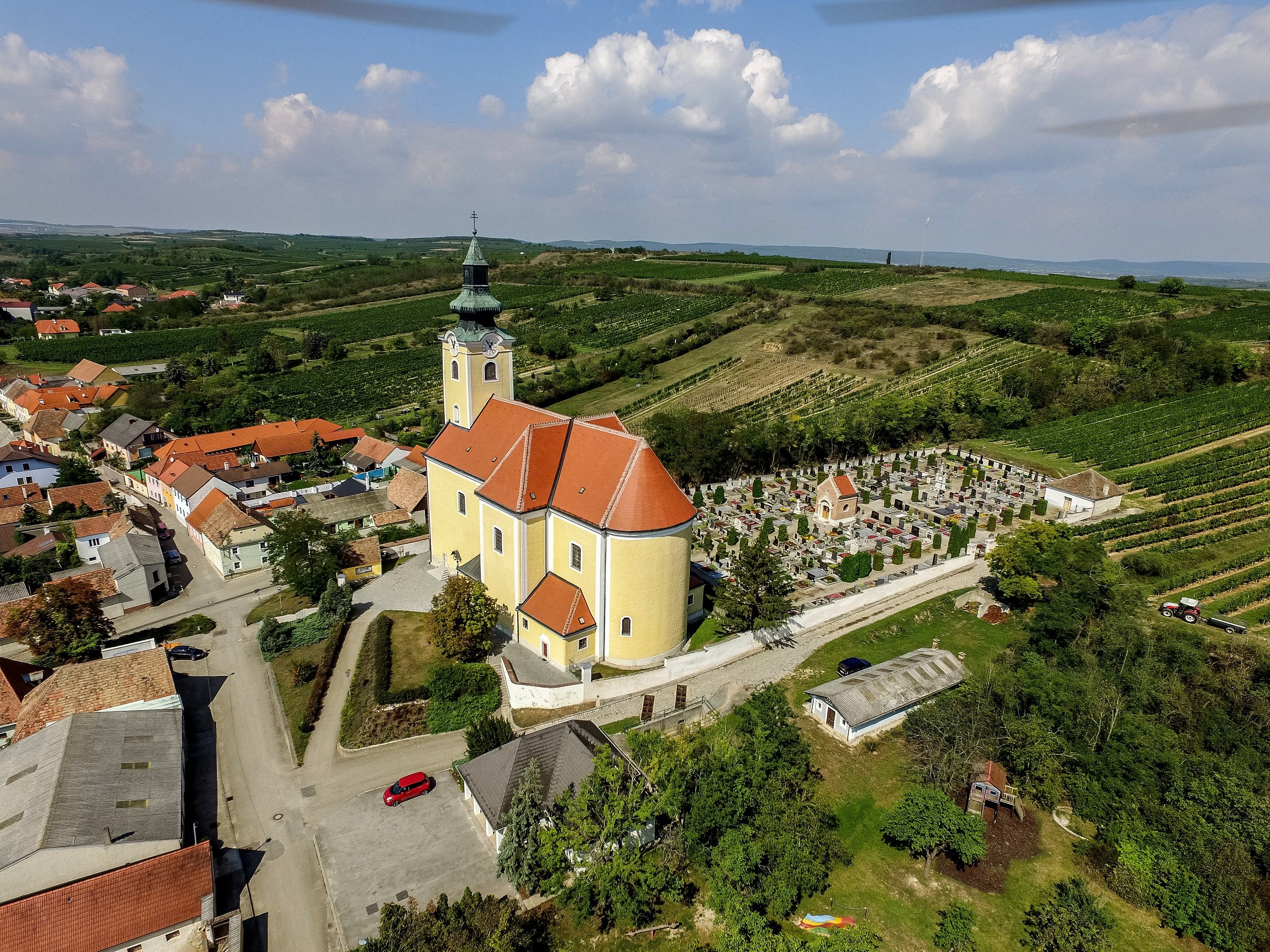 Aerial view of the parish church in Röschitz with surrounding cemetery and vineyards.