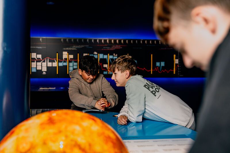 Two boys interact at a blue table in a science center.