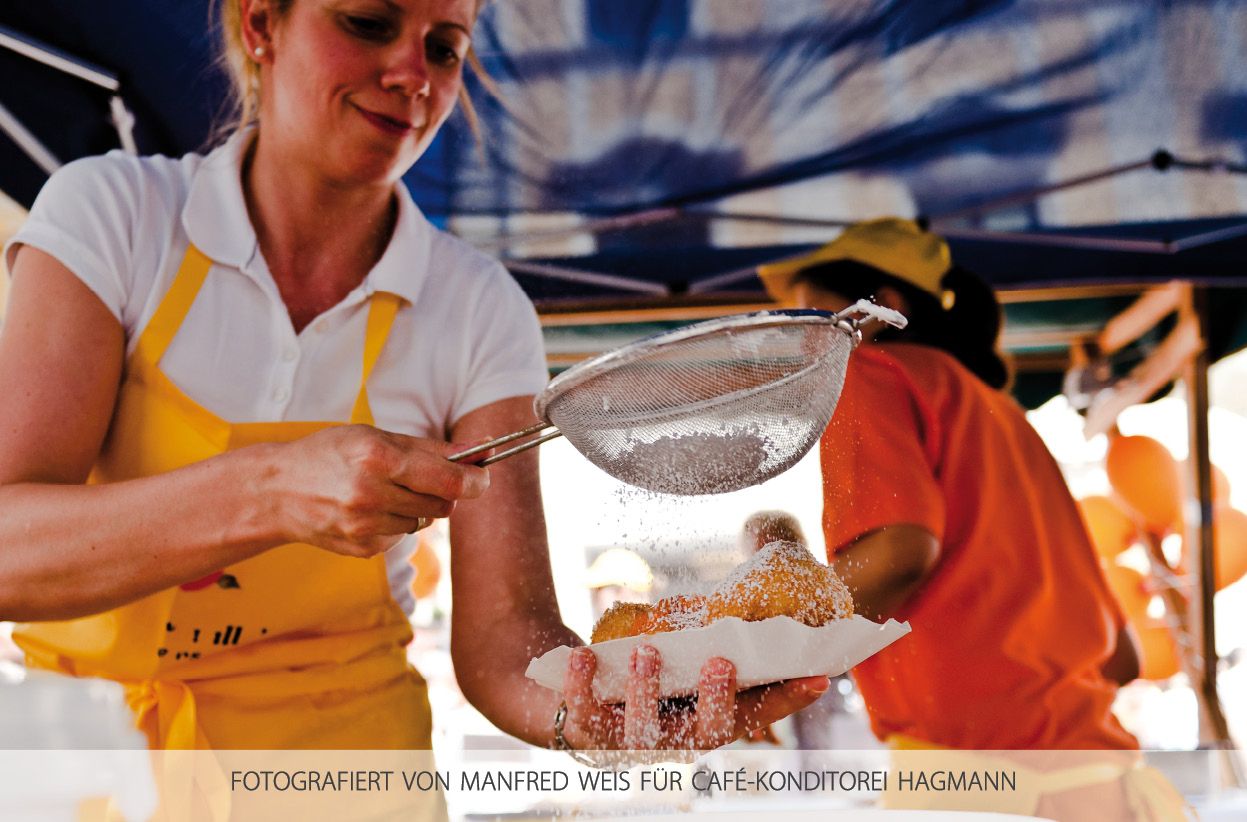 A woman dusts pastries with powdered sugar through a sieve.