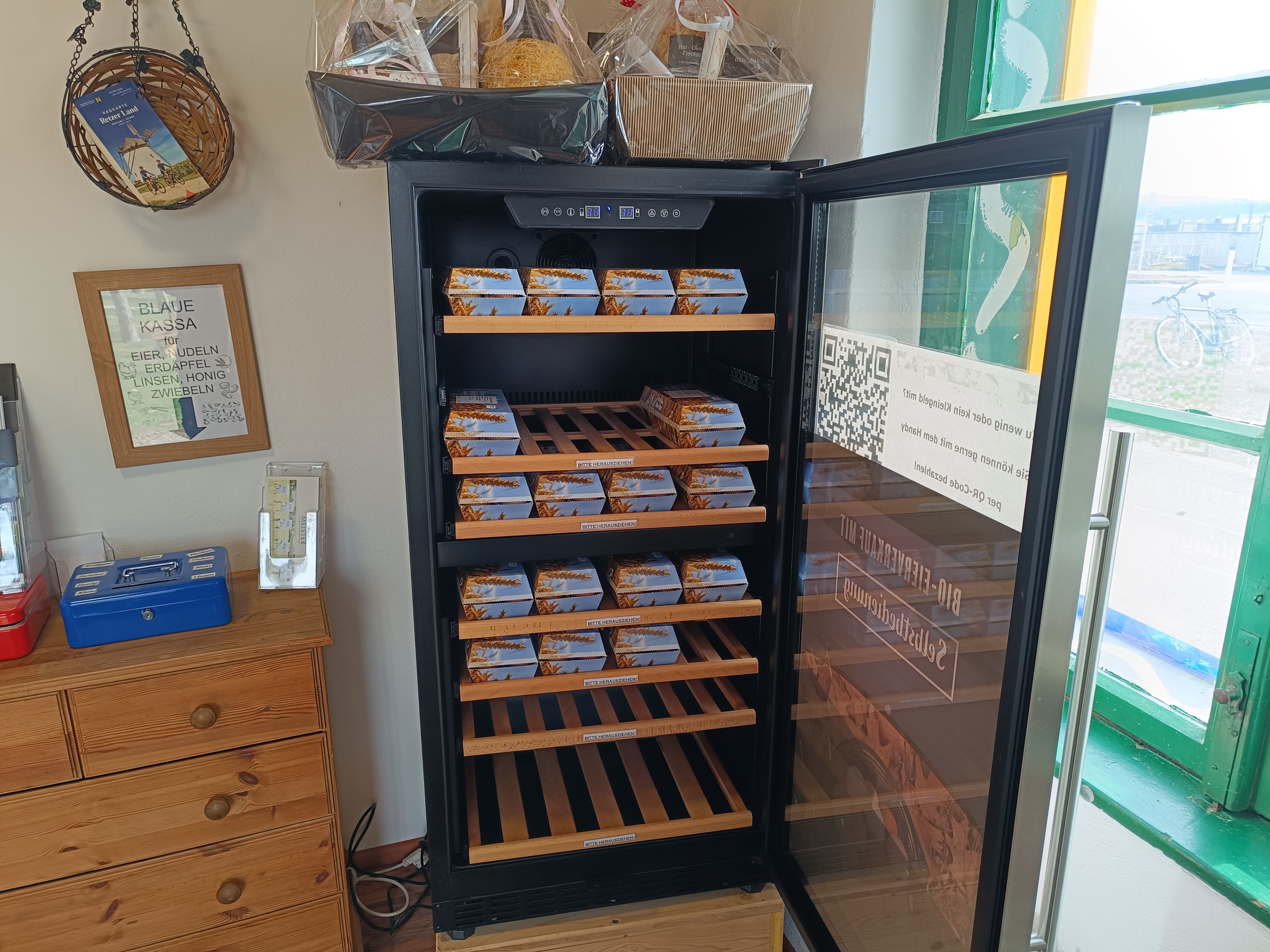 An open fridge with several packs on wooden shelves in a small store.