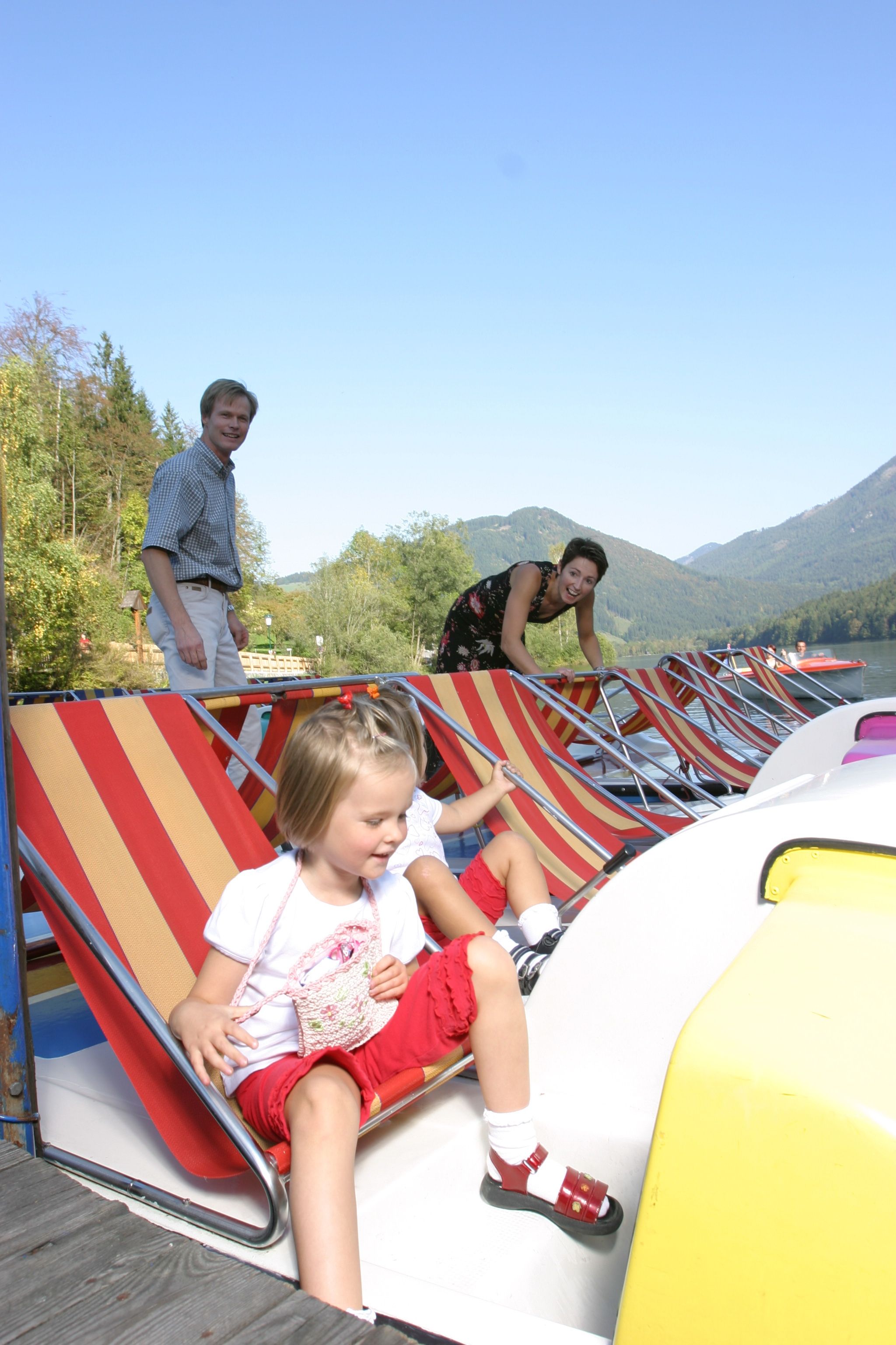 Family with children on pedal boats on a lake with mountains in the background.