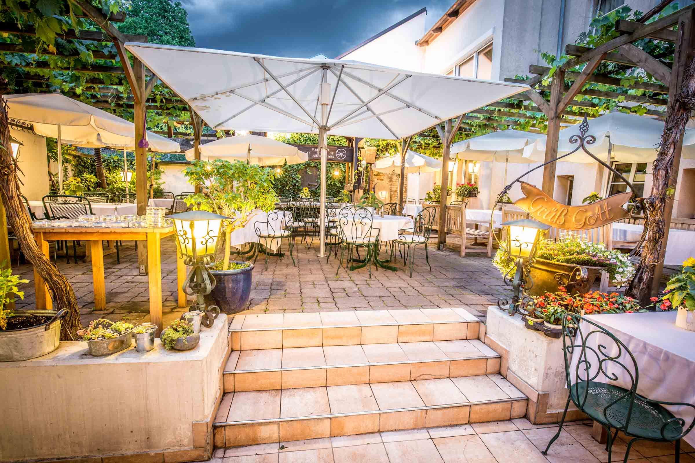 Cozy guest garden with tables, chairs and parasols, surrounded by plants and lights.