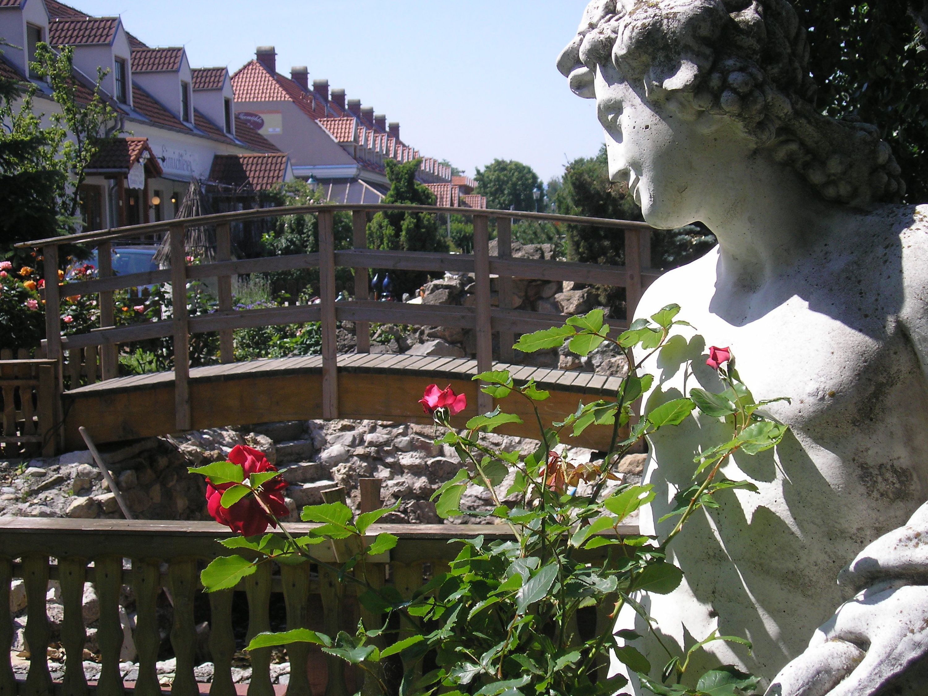 Stone statue next to a wooden bridge and red roses in the foreground.